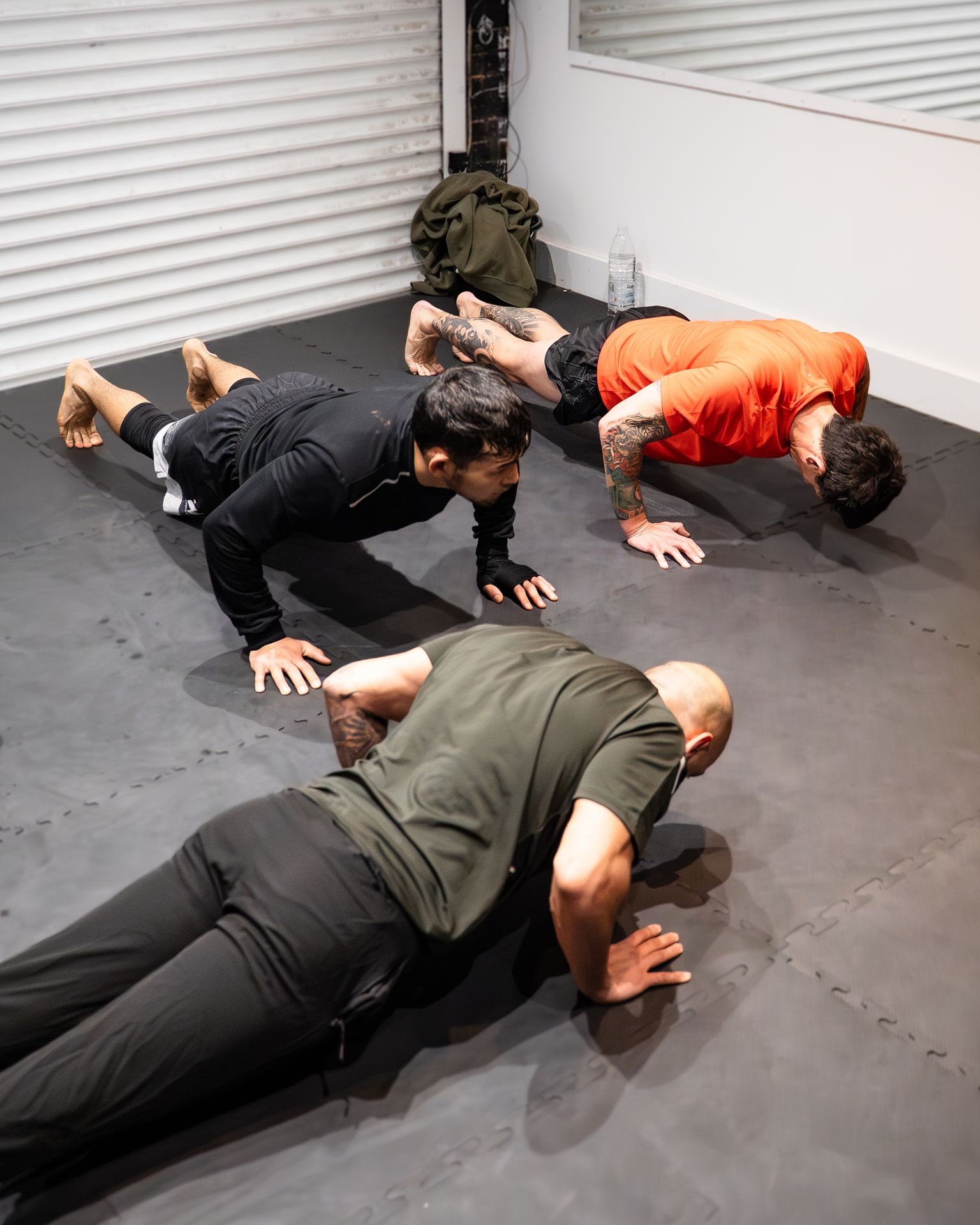 Three men performing push-ups on black gym mats in a fitness room.