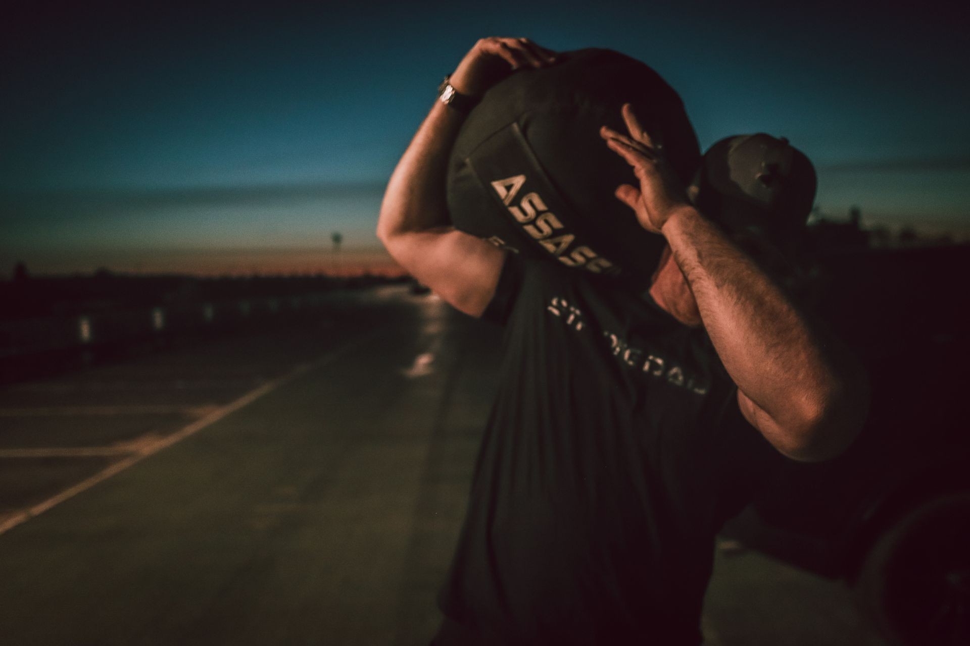 Person lifting a heavy ball overhead during sunset, with an empty road in the background.