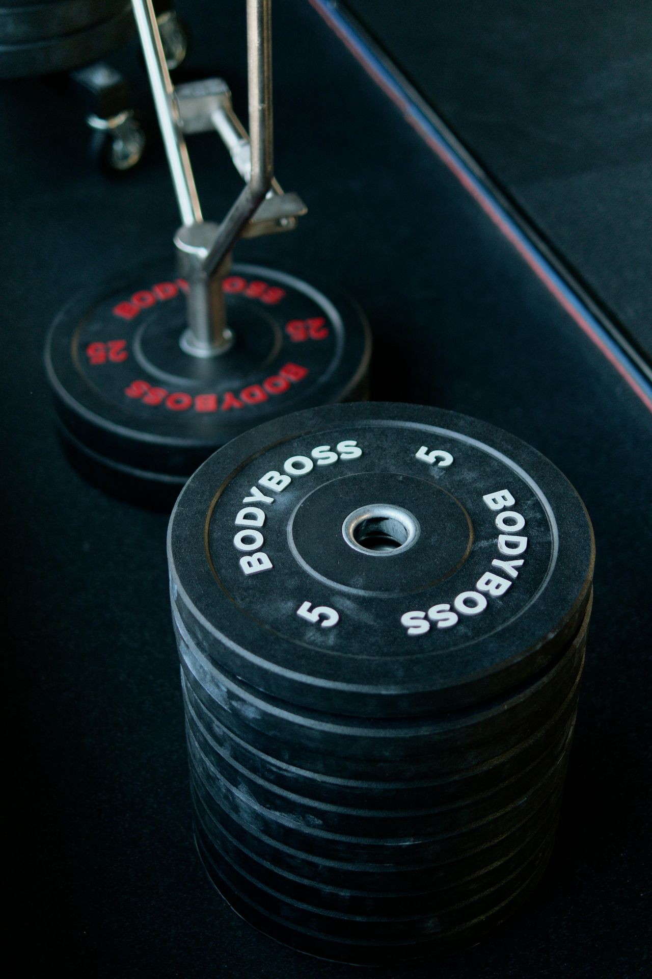 Stack of Bodyboss weight plates and a partially visible barbell in a gym setting.