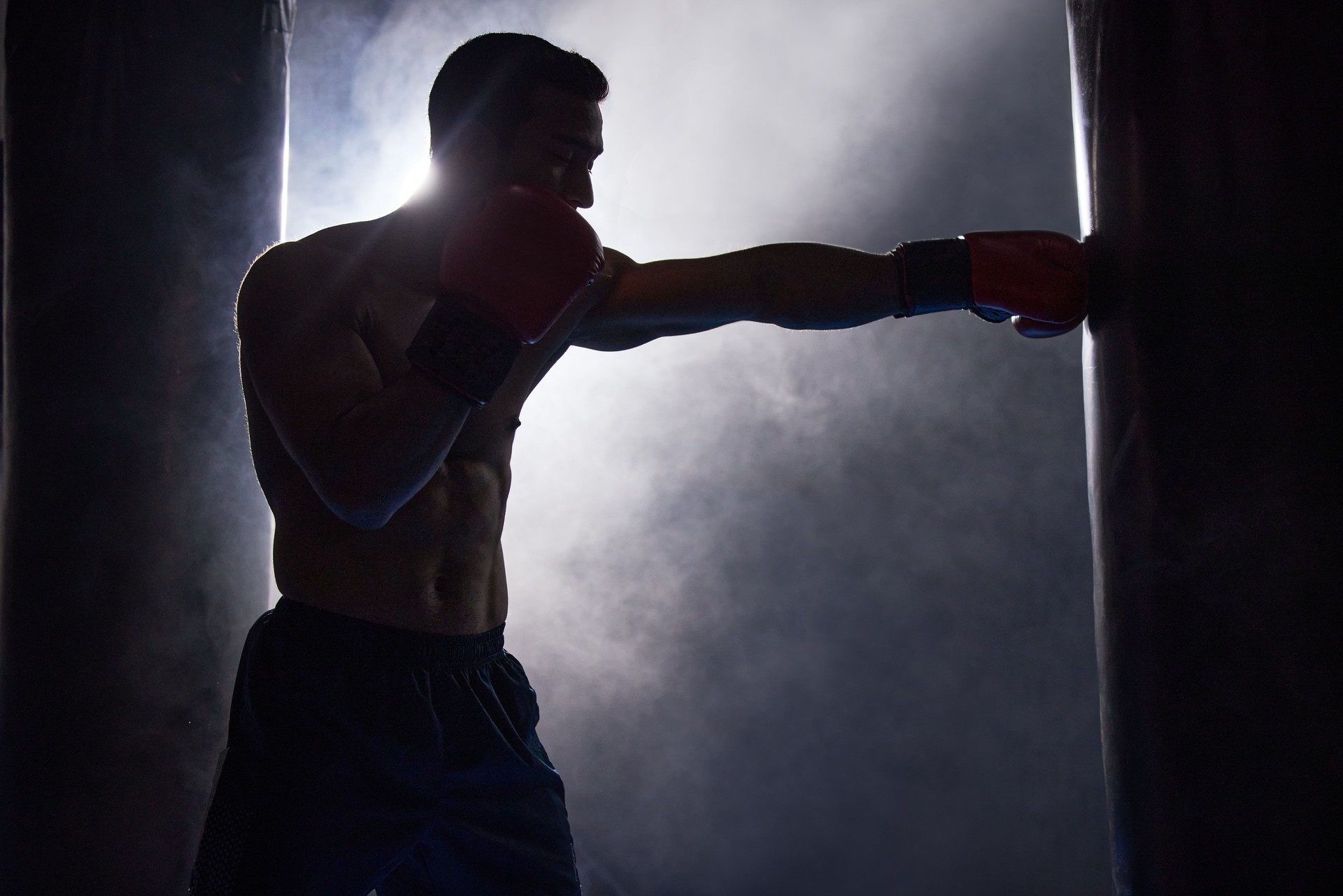Cropped shot of a silhouetted young male boxer working out on a punching bag in the gym