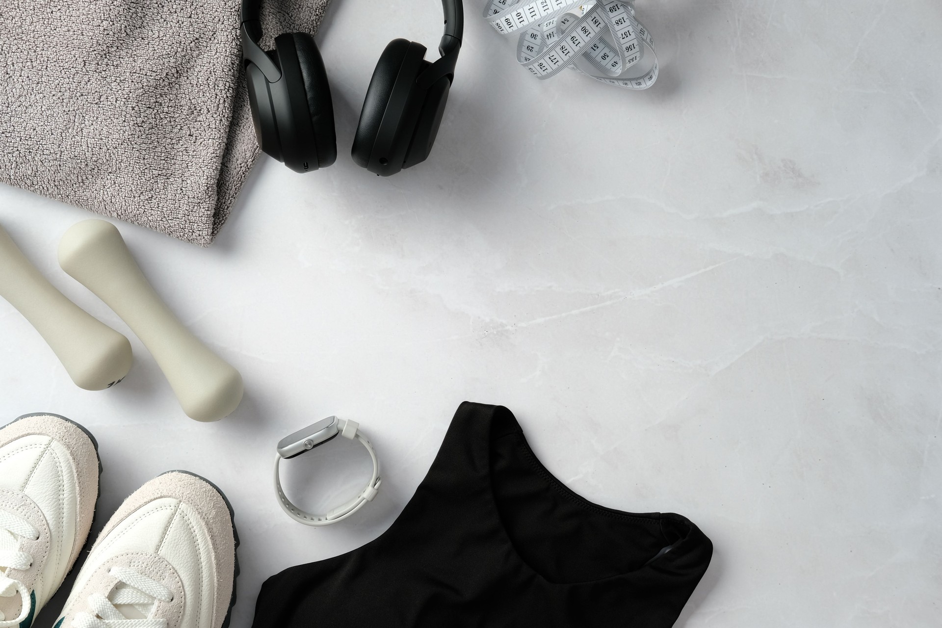 Fitness flat lay: dumbbells, sneakers, sports top, tracker, headphones, towel, measuring tape on marble background. Workout, sport, healthy lifestyle concept. Copy space.